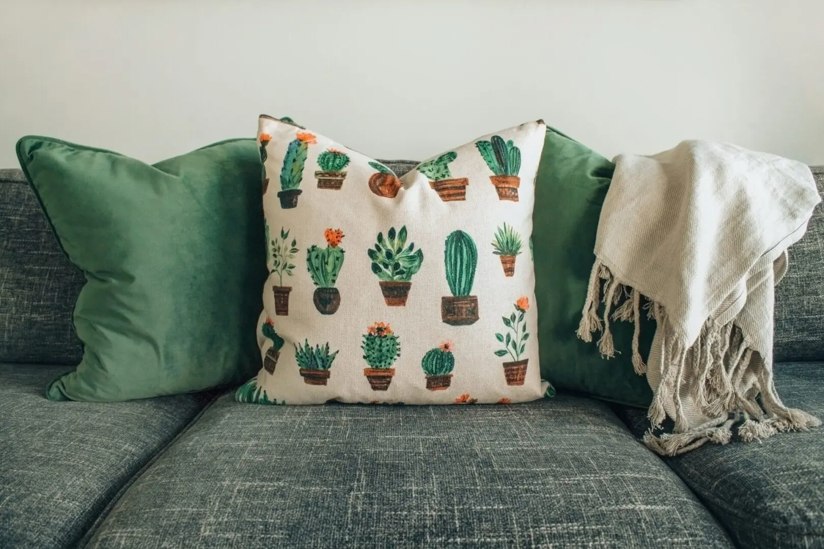 A couch with two pillows and one has cactus on it.