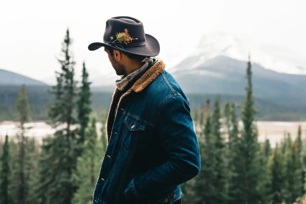 A man in a hat and jacket standing on top of a hill.