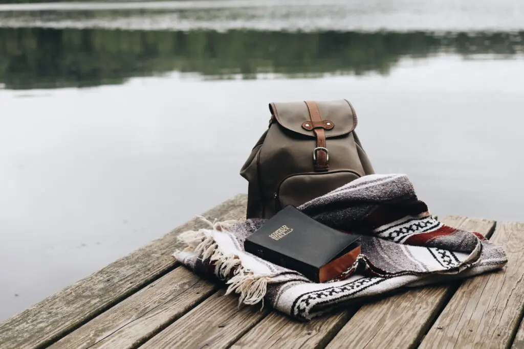 A backpack and book on the dock by the water.