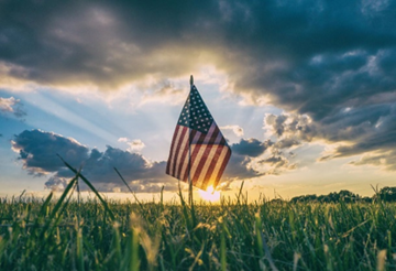 A flag is in the grass under cloudy skies.