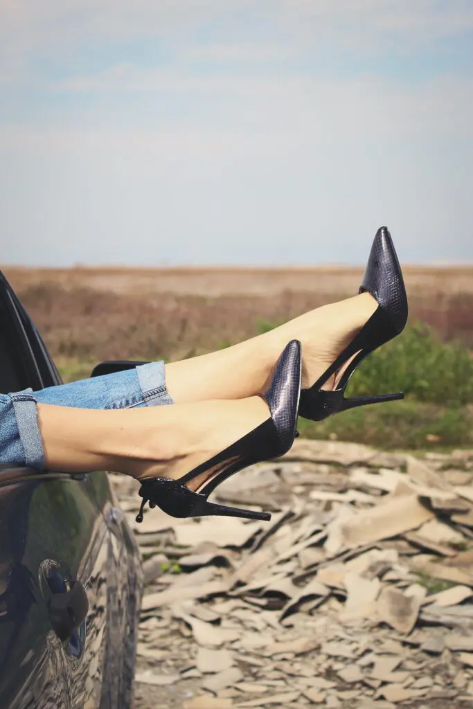 A woman 's legs in high heels are sticking out of the trunk of her car.