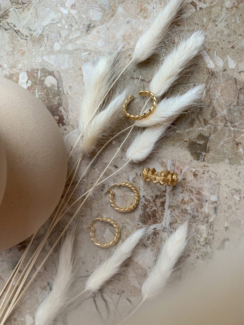 A hat and some small gold hoops on top of a bunch of dried flowers.