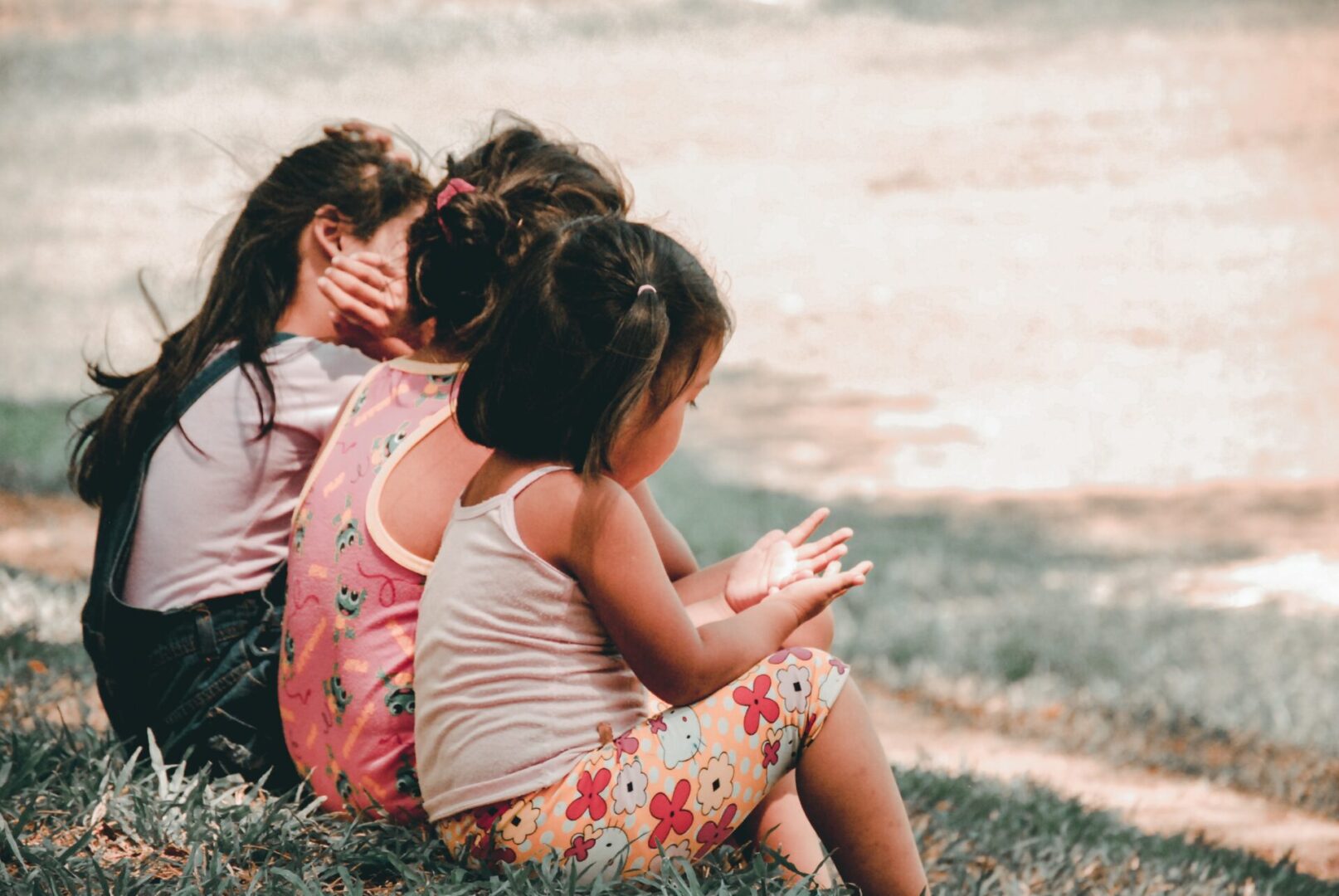 Three children sitting on the grass looking at their phones.