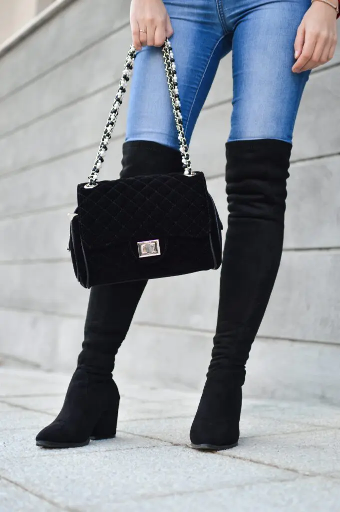 A woman wearing black boots and carrying a purse.