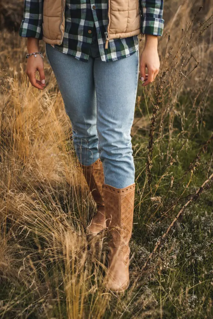 A woman in boots and jeans standing on top of a hill.